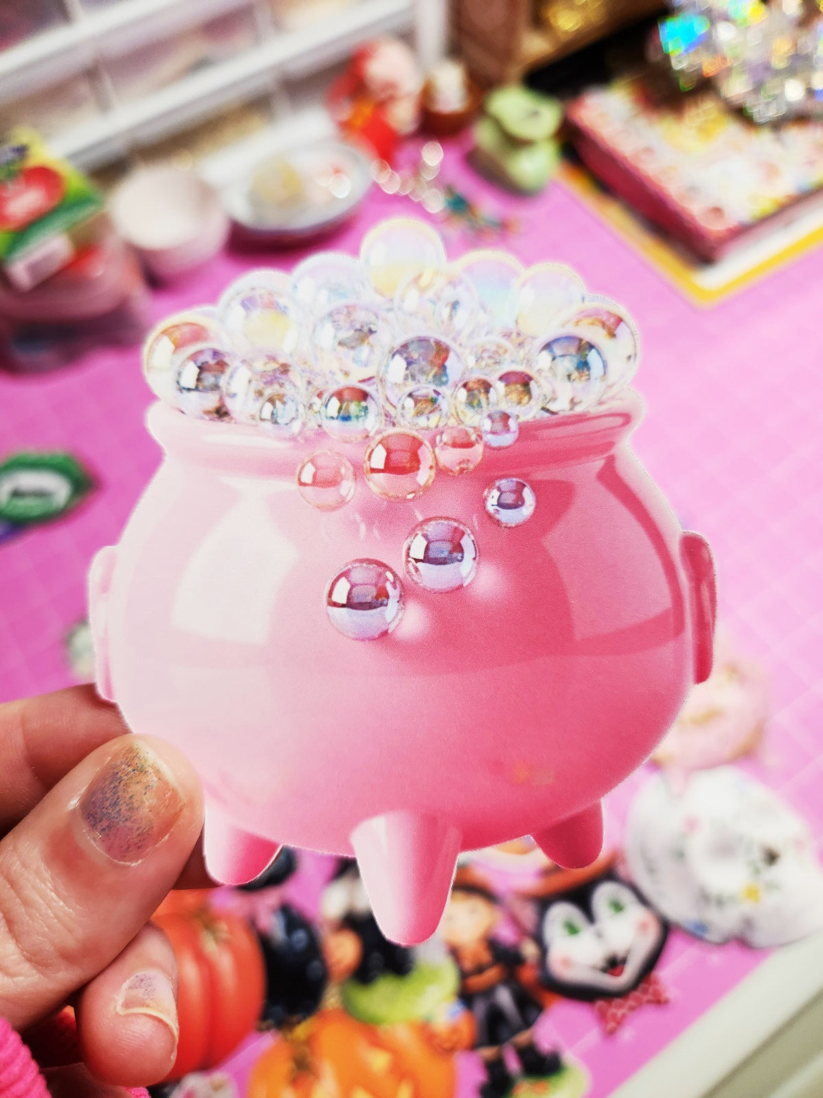 Pink decorative item with rhinestones held by a hand against a colorful background