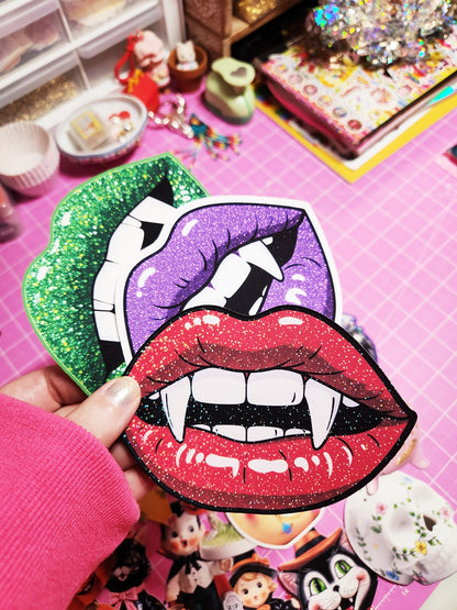 Colorful glittery lips patch held by a hand on a pink surface with toys in the background