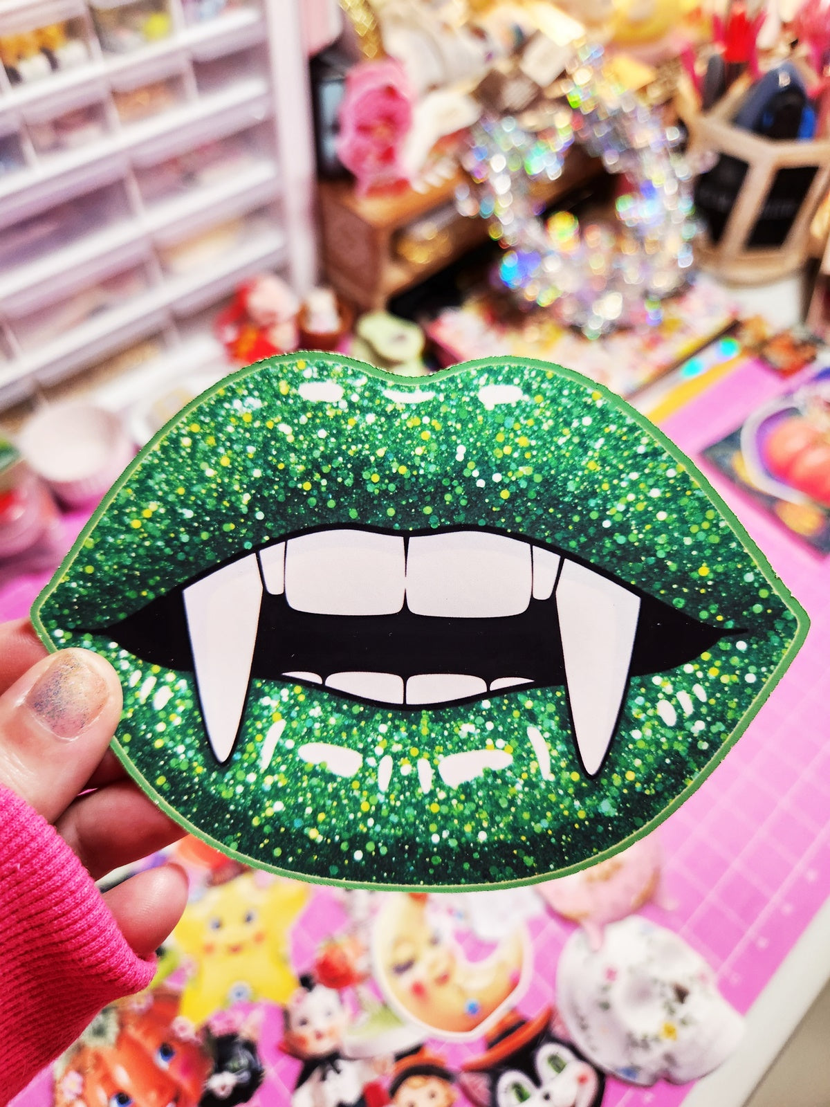 Green glittery lip-shaped object with vampire teeth held in front of a colorful background.