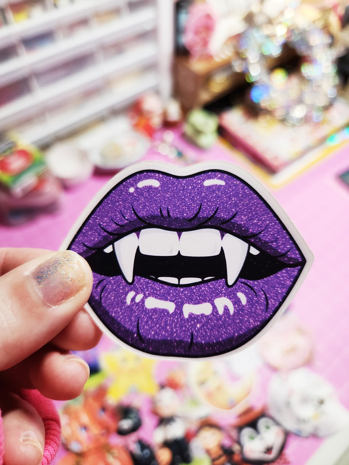 Purple glittery lips with fangs patch held by a hand against a colorful background