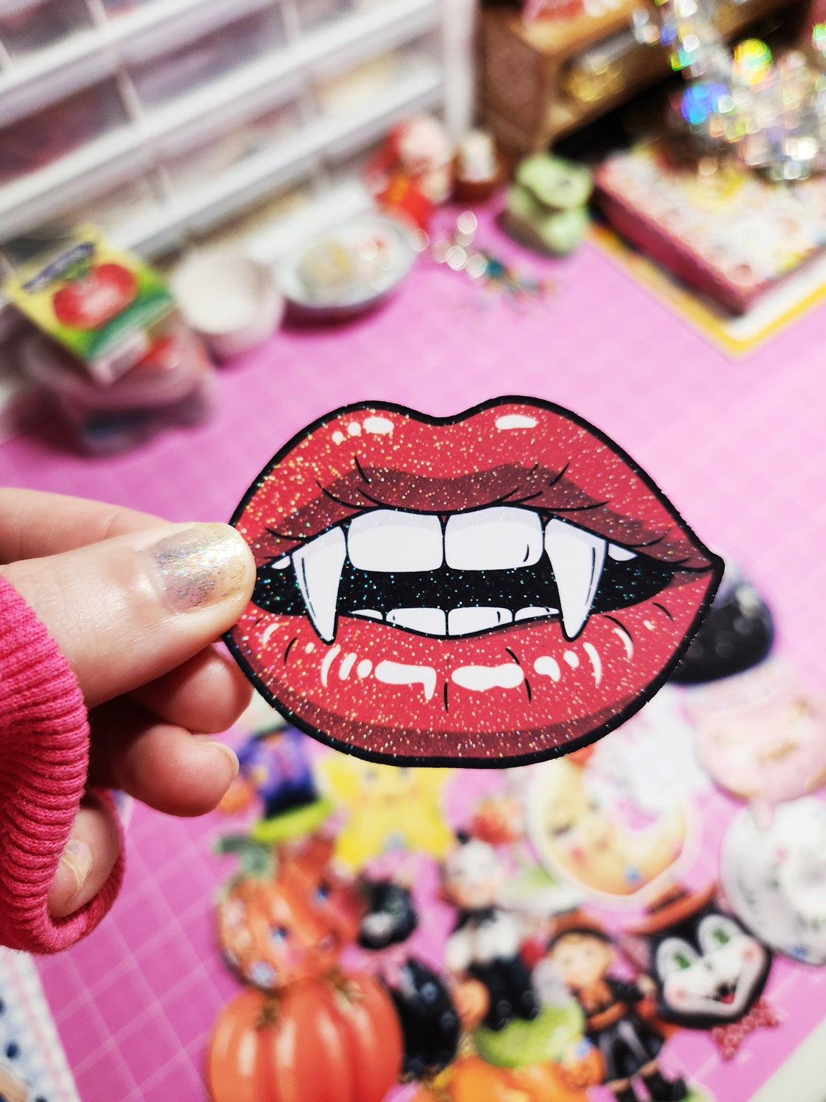 Lip patch with vampire design held by a hand against a colorful, blurred background