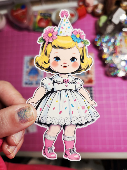 Cartoon character sticker with a colorful dress and party hat held against a pink background.