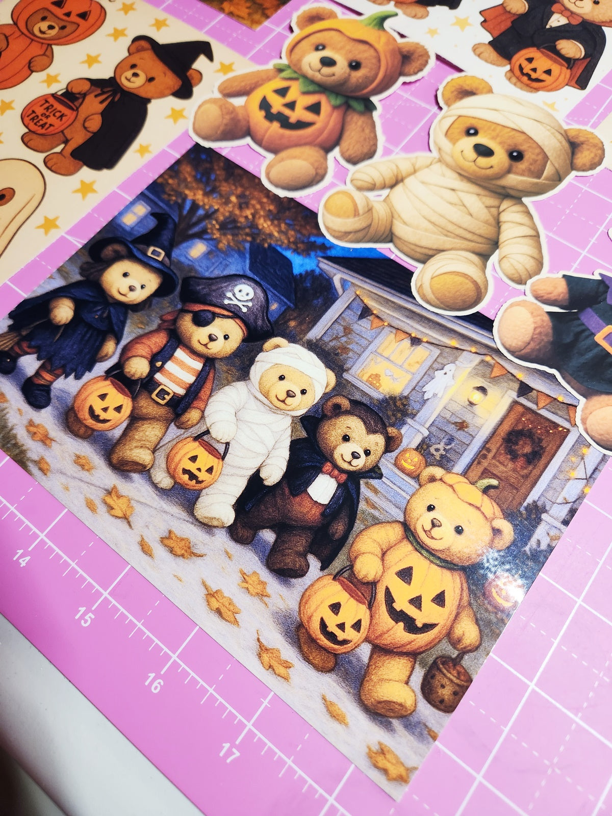 Halloween-themed teddy bear stickers on a pink cutting mat with grid lines.