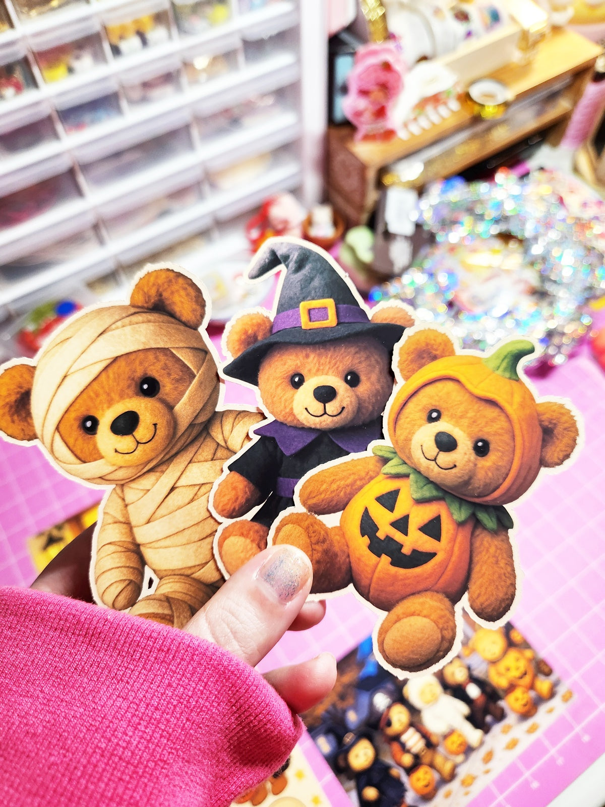 Three Halloween-themed teddy bears held by a hand in a store setting.