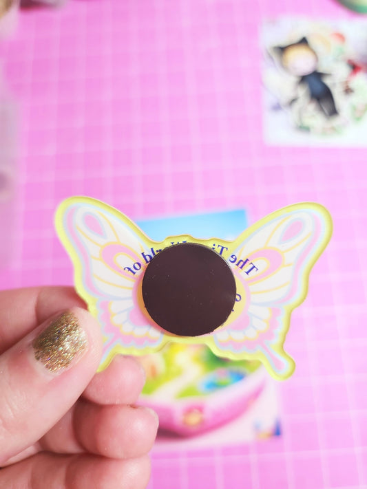 Butterfly-shaped magnet with a hand holding it against a pink background