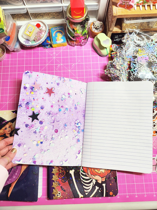 Notebook with colorful cover held over a pink cutting mat with various items.