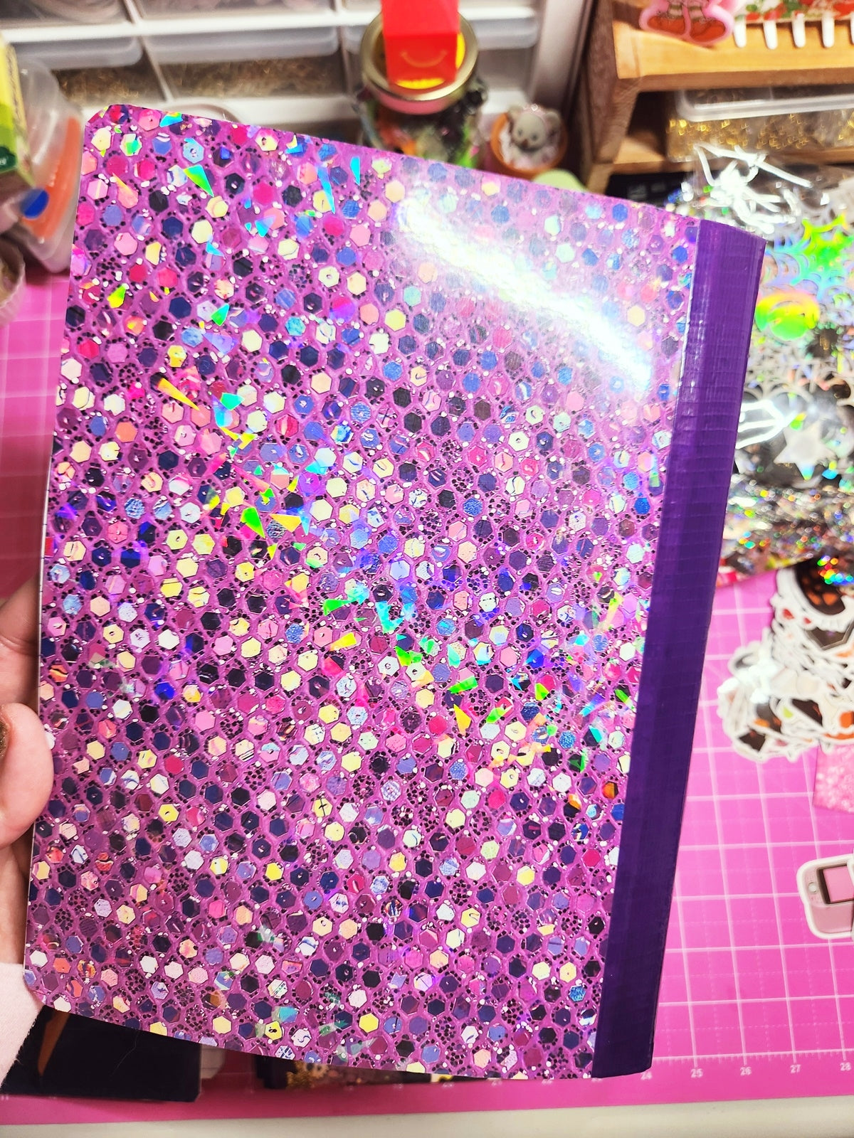Glittery pink notebook held by a hand on a colorful background