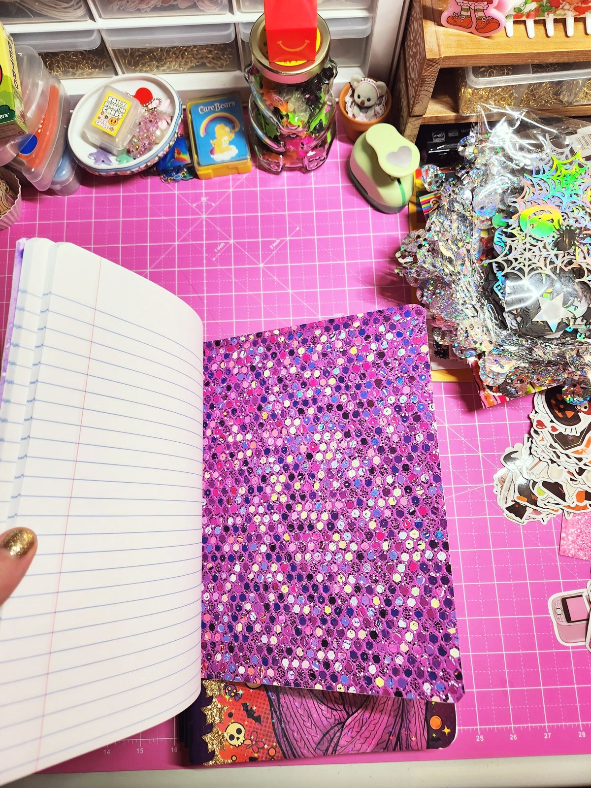 Open notebook on a pink cutting mat with various items around