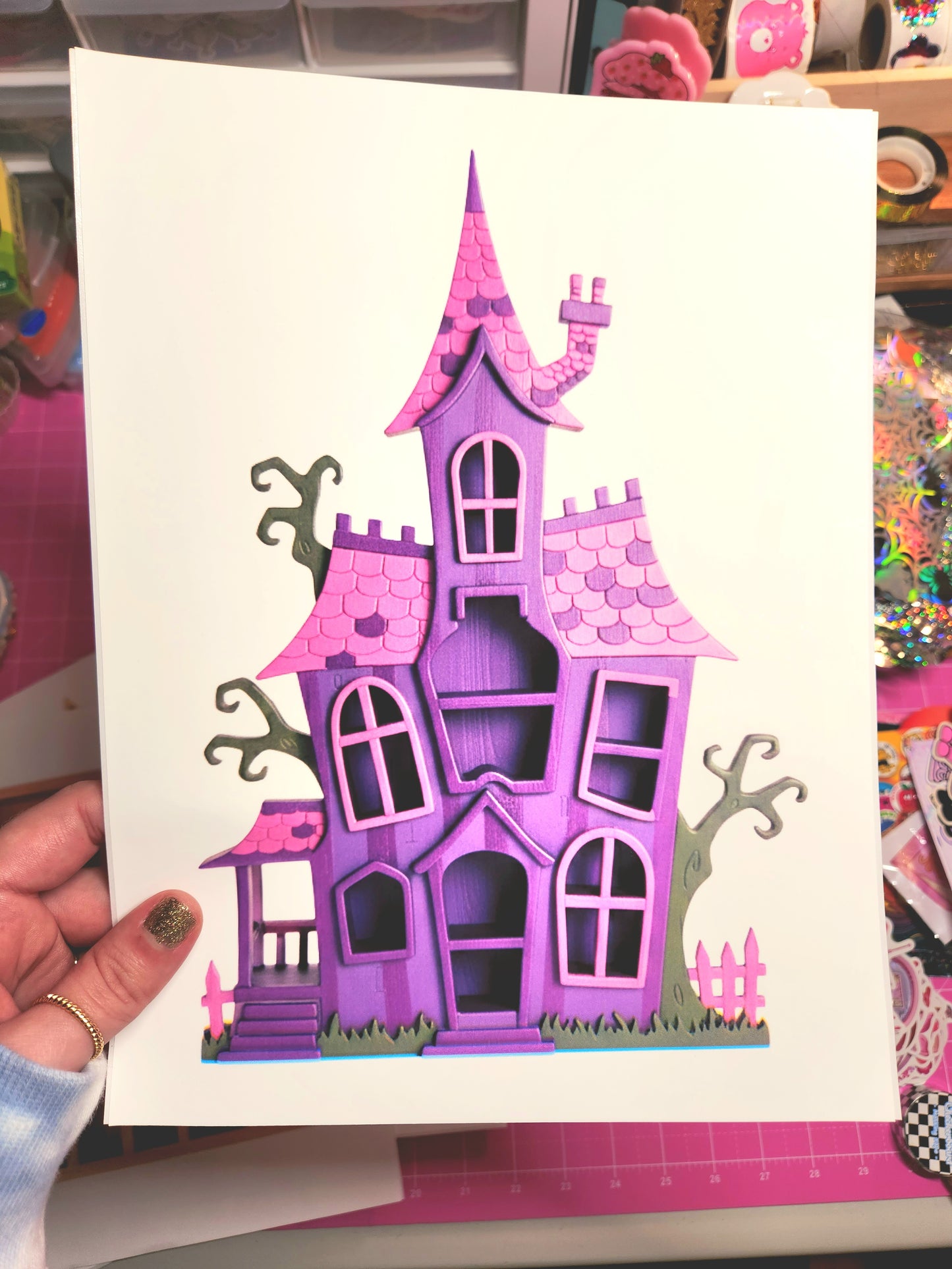 Hand holding a card with a purple haunted house design on a colorful background