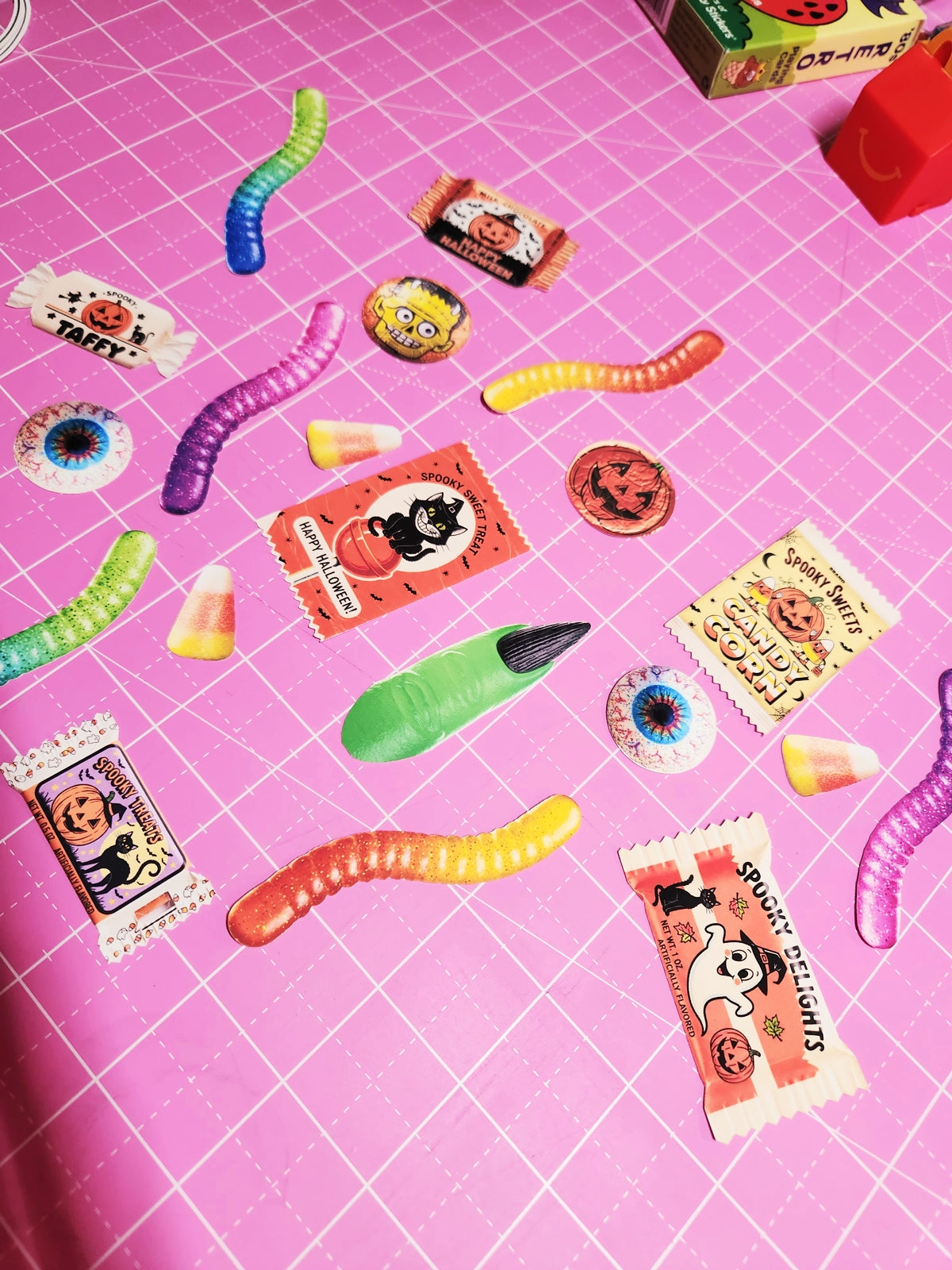 Halloween-themed candy and toy items on a pink grid background