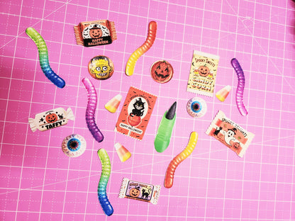 Halloween-themed candy and gummy worms on a pink grid background