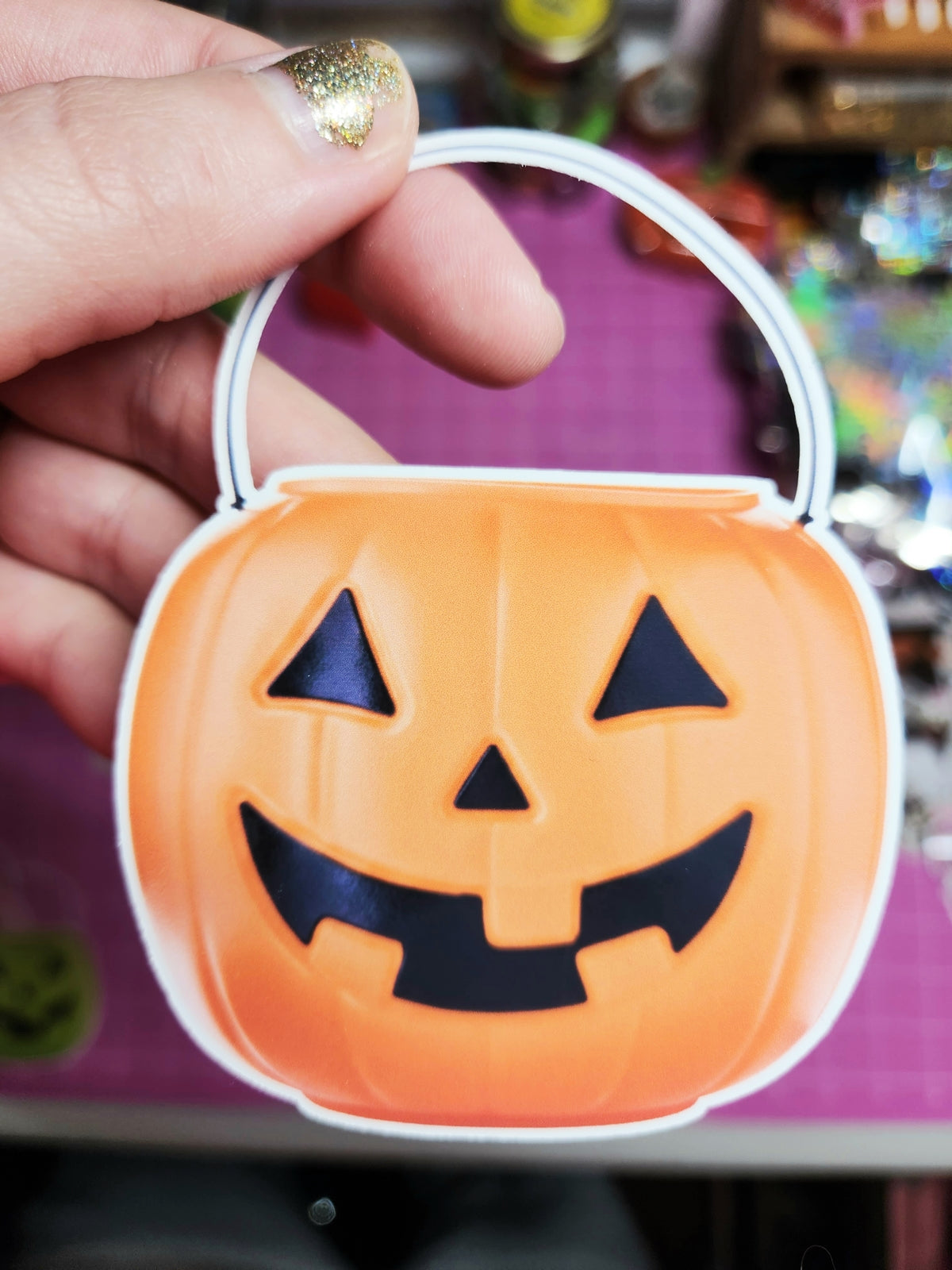 Halloween-themed candy container with a pumpkin face design held by a hand.