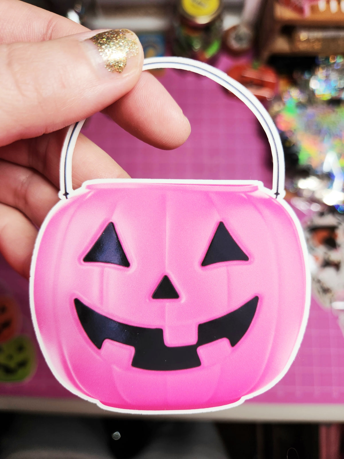 Pink Halloween candy basket with black jack-o'-lantern face design held by a hand.