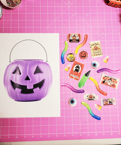 Purple Halloween candy bucket with small decorations on a pink cutting mat
