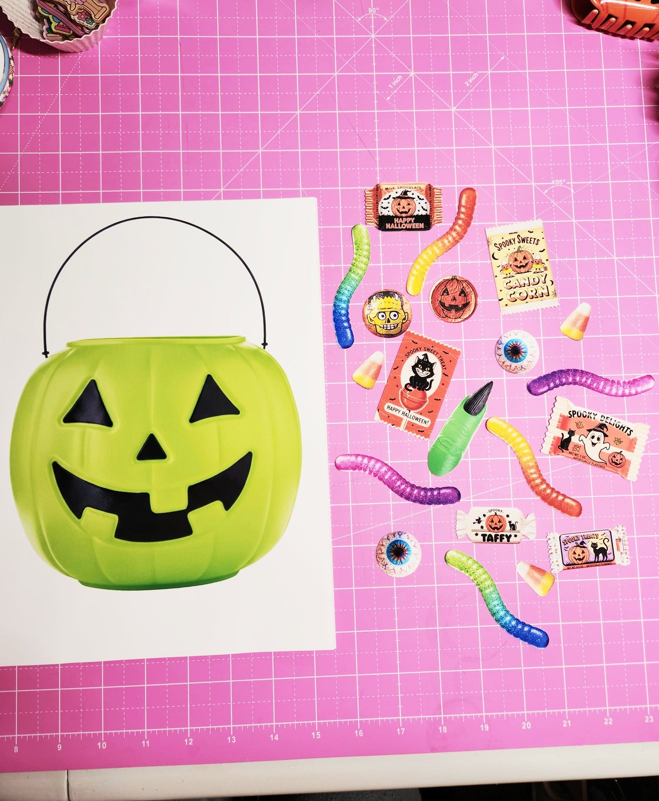 Green Halloween candy bucket with small decorations on a pink grid background