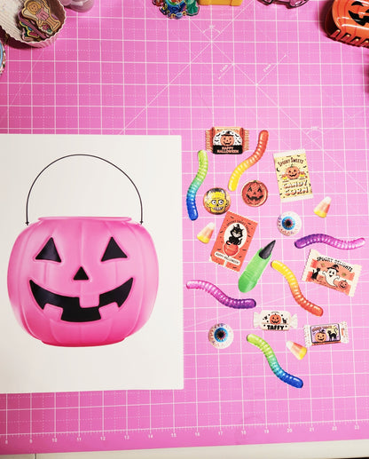 Pink Halloween candy bucket with accessories on a pink grid background