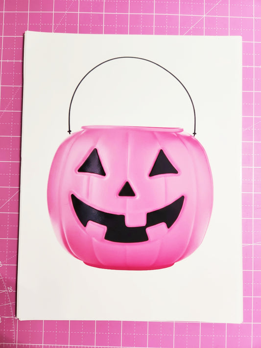 Pink Halloween candy bucket with black jack-o'-lantern face on a pink grid background