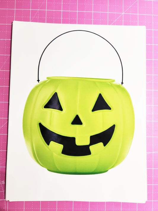 Green Halloween candy bucket with a jack-o'-lantern face on a pink grid background