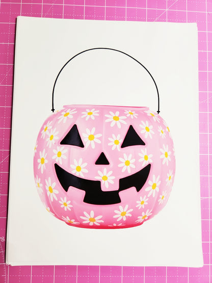Pink Halloween candy bucket with black jack-o'-lantern face design on a pink grid background