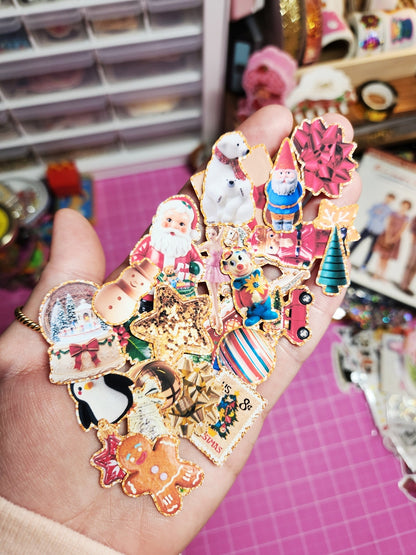 Hand holding various colorful Christmas-themed pins with a blurred craft store background.