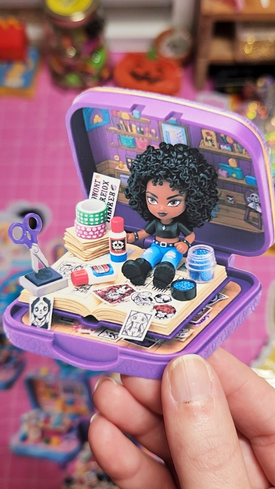 Small figurine with accessories in a purple case held by a hand on a colorful background