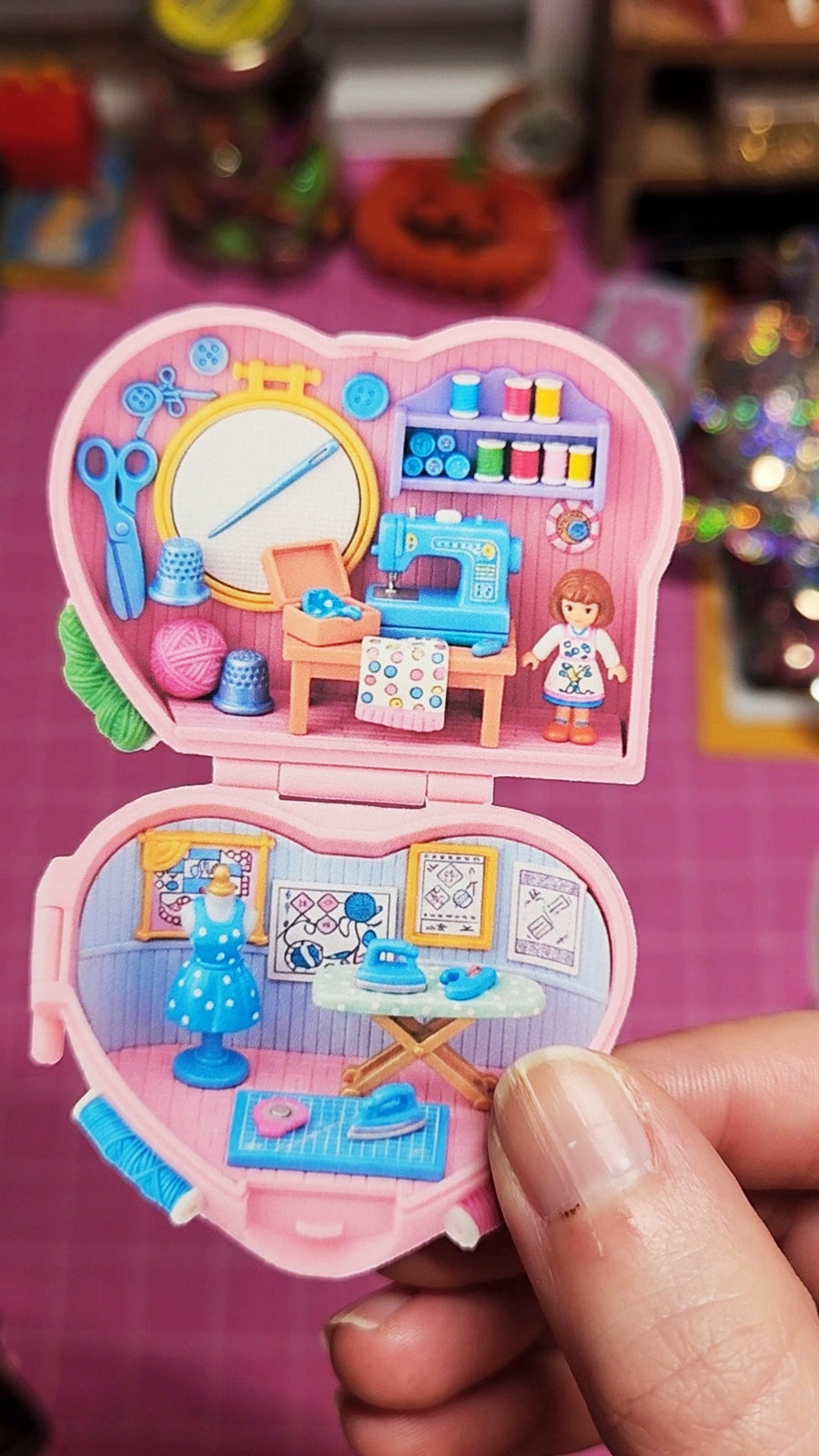 Toy heart-shaped playset with miniature room inside, held by a hand.