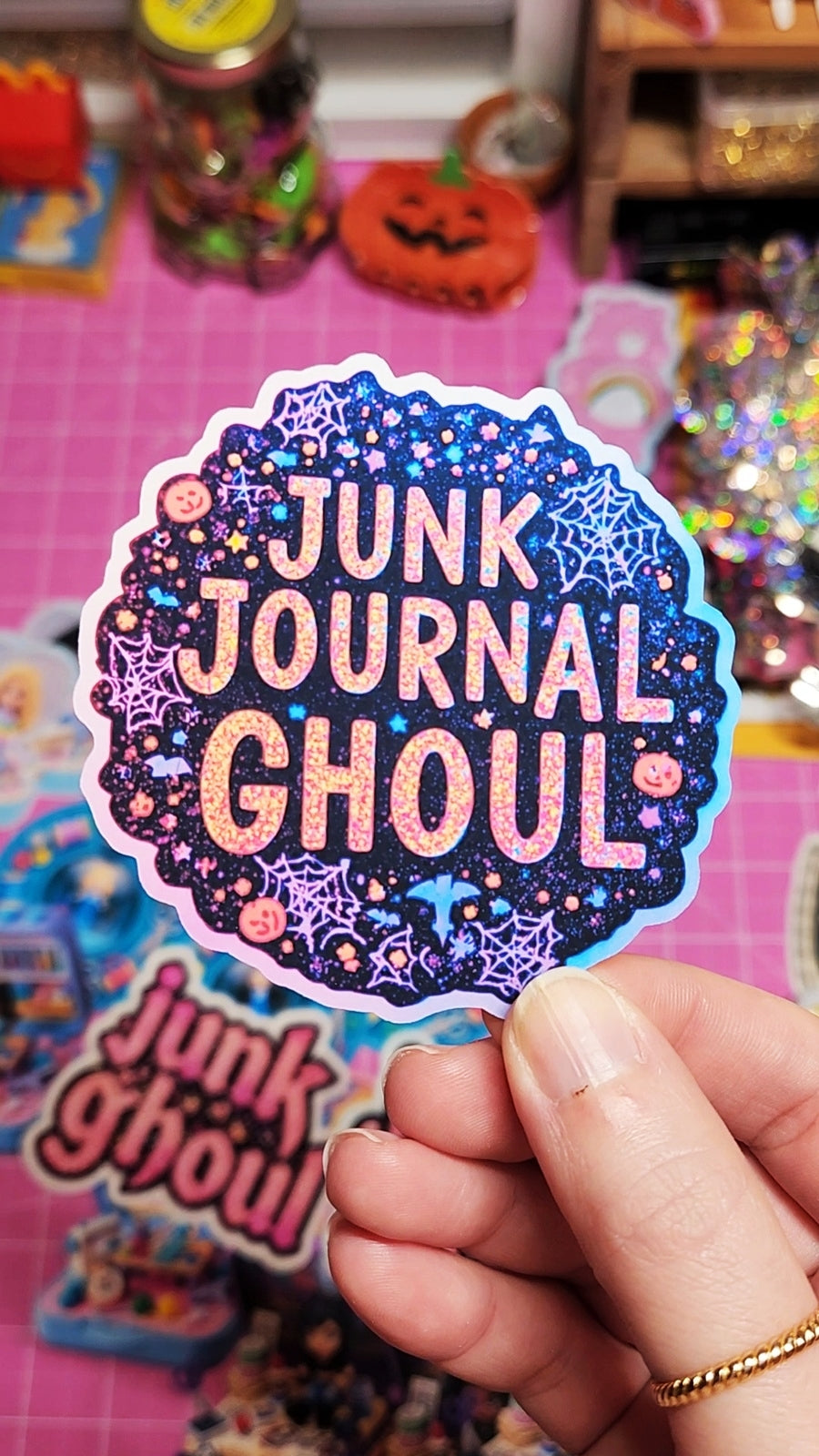 Sticker with 'Junk Journal Ghoul' text held by a hand against a colorful background.