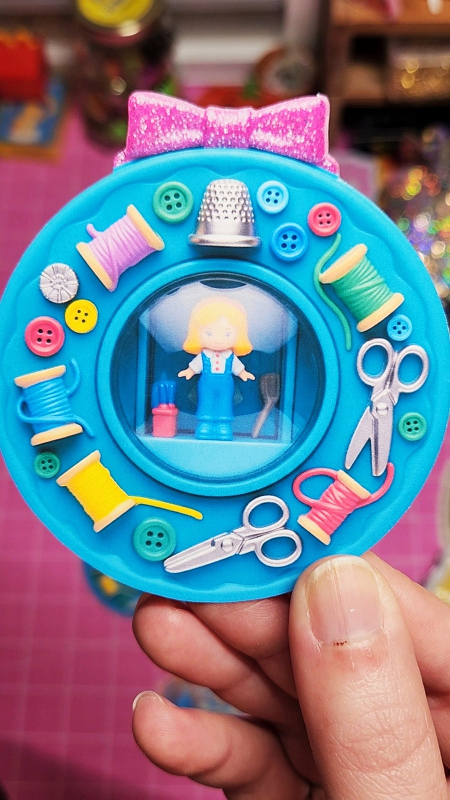 Toy sewing set with a character inside, held by a hand on a colorful background