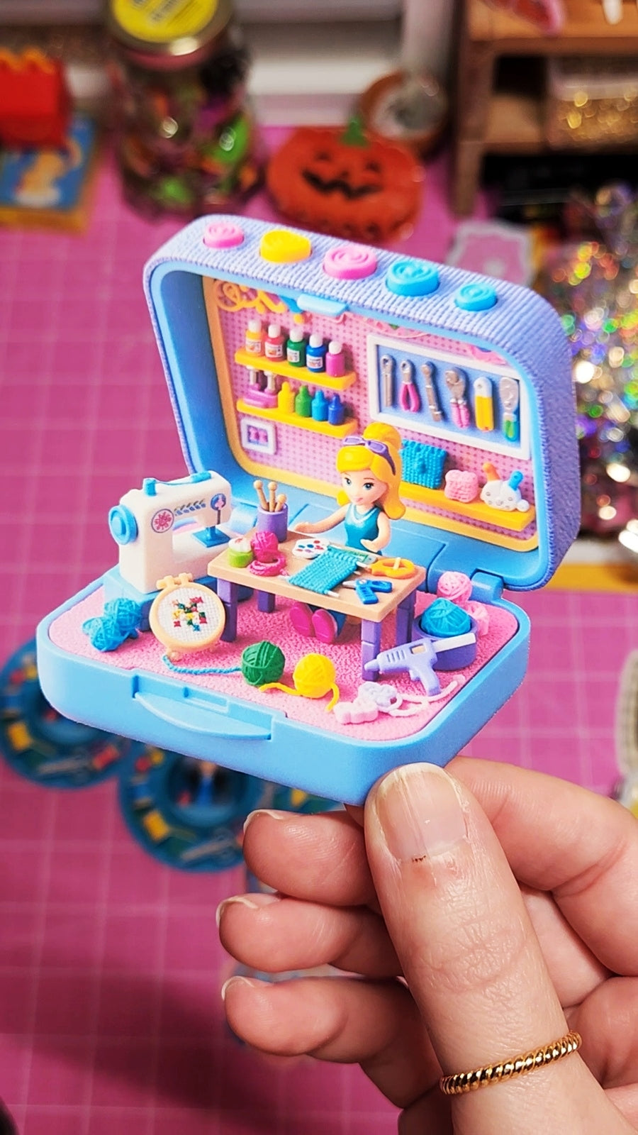 Toy jewelry box with a colorful interior scene held by a hand on a pink surface.