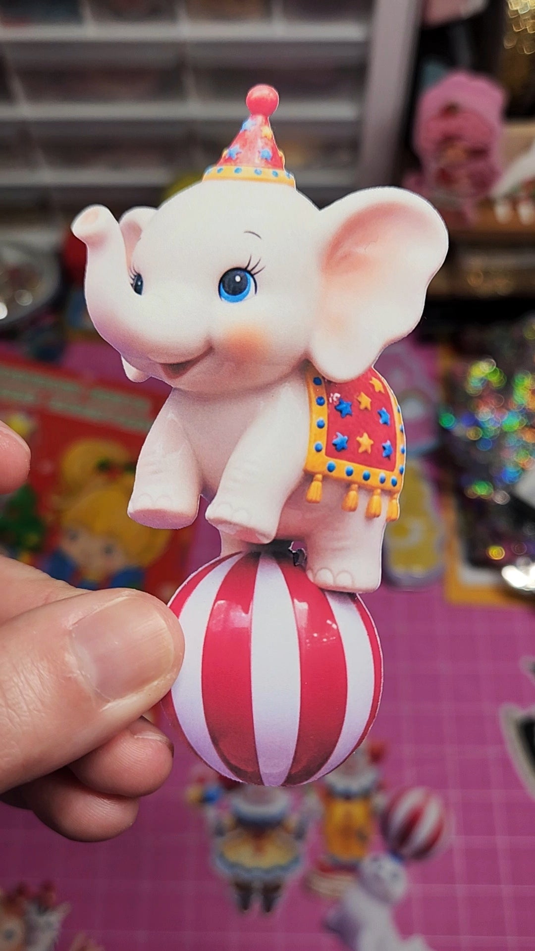 Toy elephant on a striped ball held by a hand with a colorful background