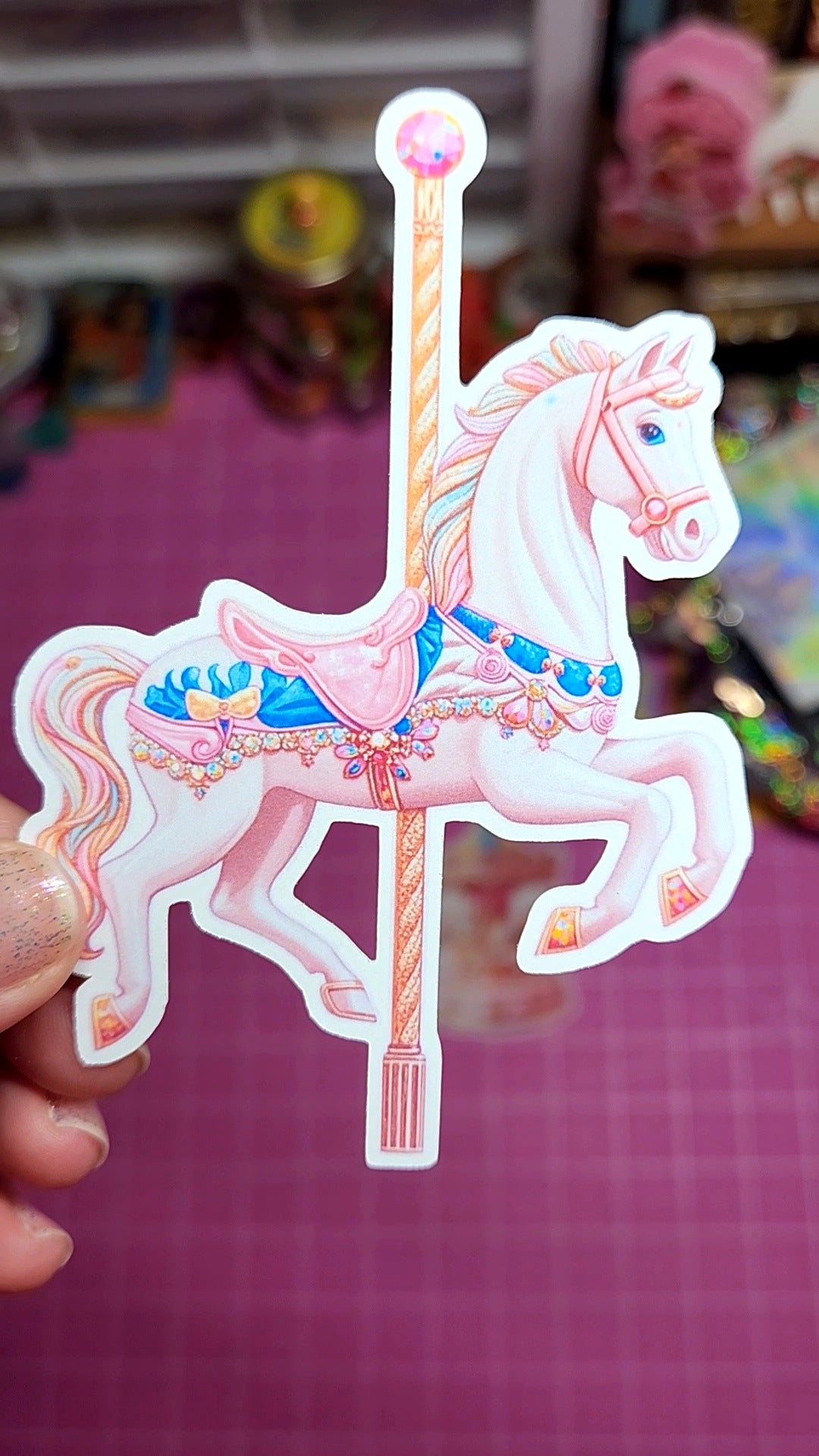 Decorative sticker of a carousel horse held by a hand on a pink background.