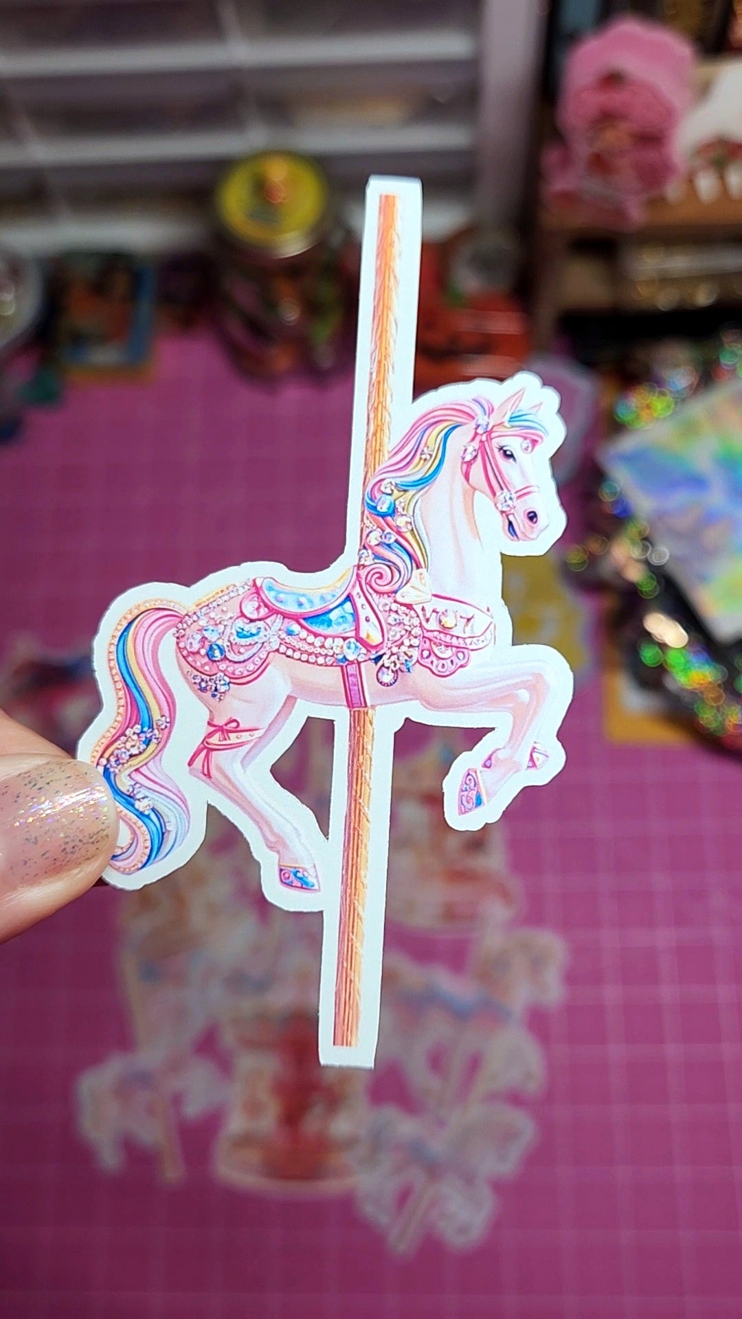 Sticker of a carousel horse held by a hand with a colorful background.