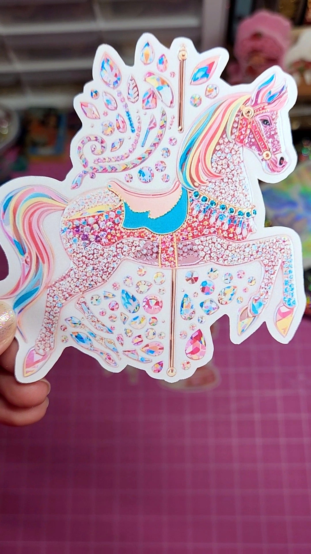 Colorful sticker of a carousel horse held by a hand on a checkered background