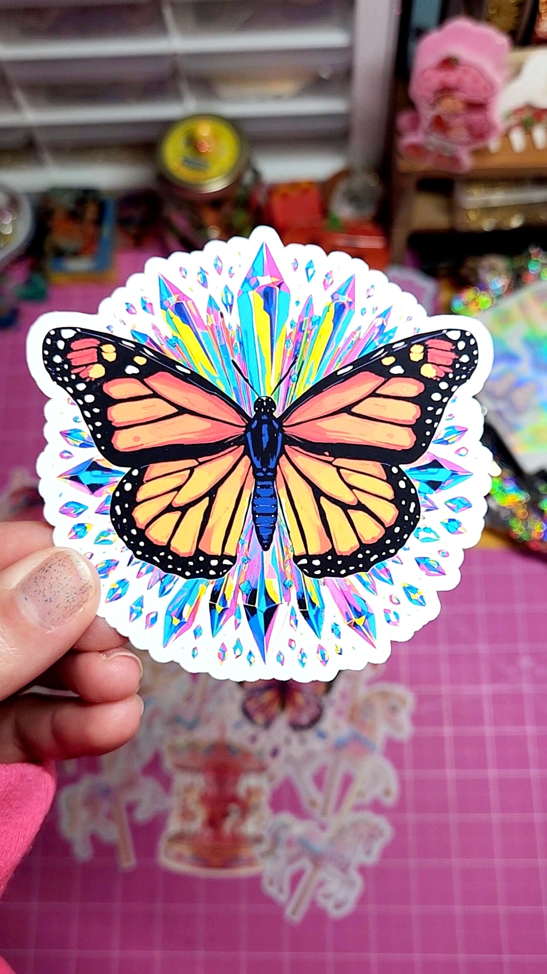 Colorful butterfly sticker held by a hand on a pink grid background