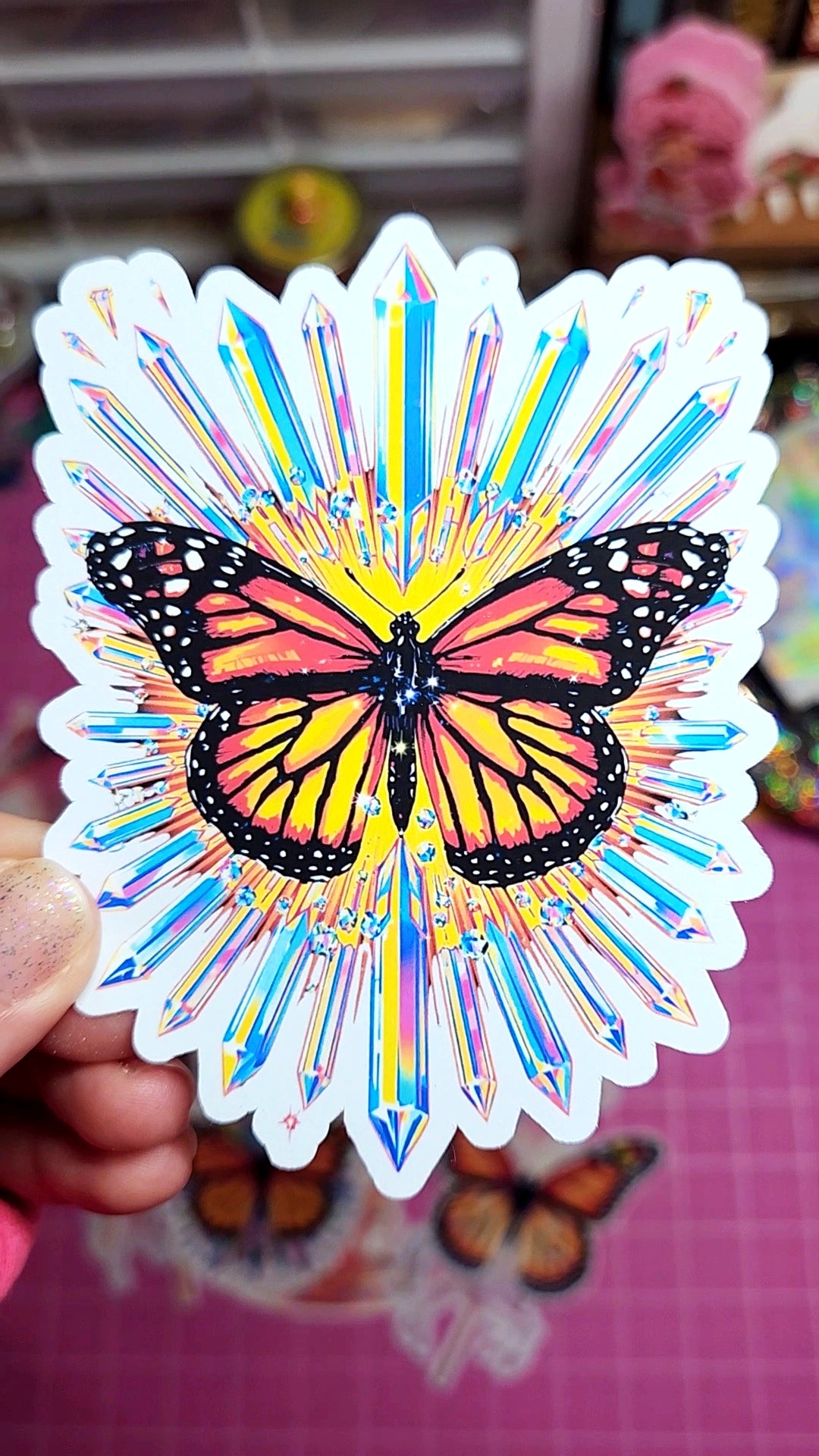 Colorful butterfly sticker with放射性设计 held by a hand on a pink surface.