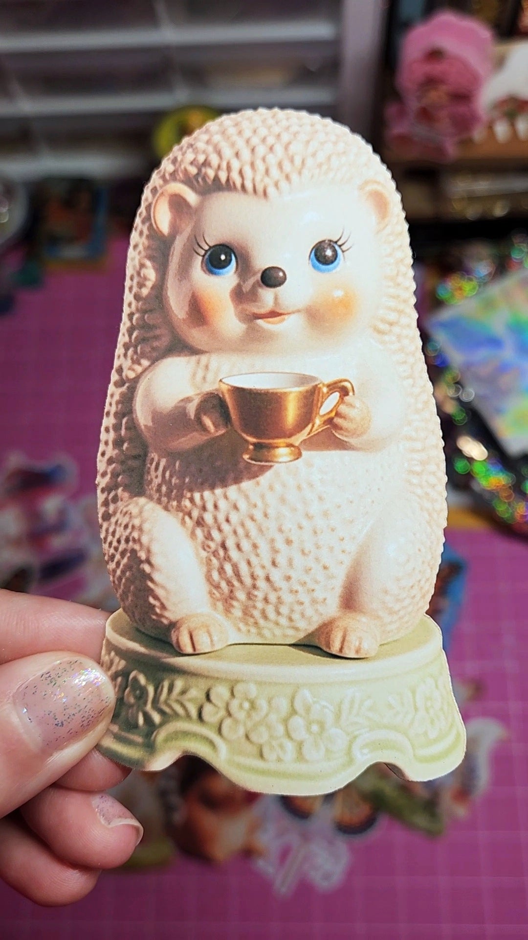 Hedgehog figurine holding a cup with a person's hand holding it, on a colorful background.
