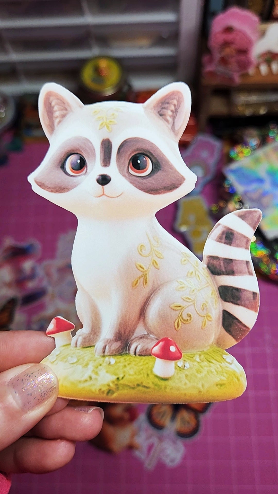 Cartoon raccoon figurine held by a hand with a colorful background