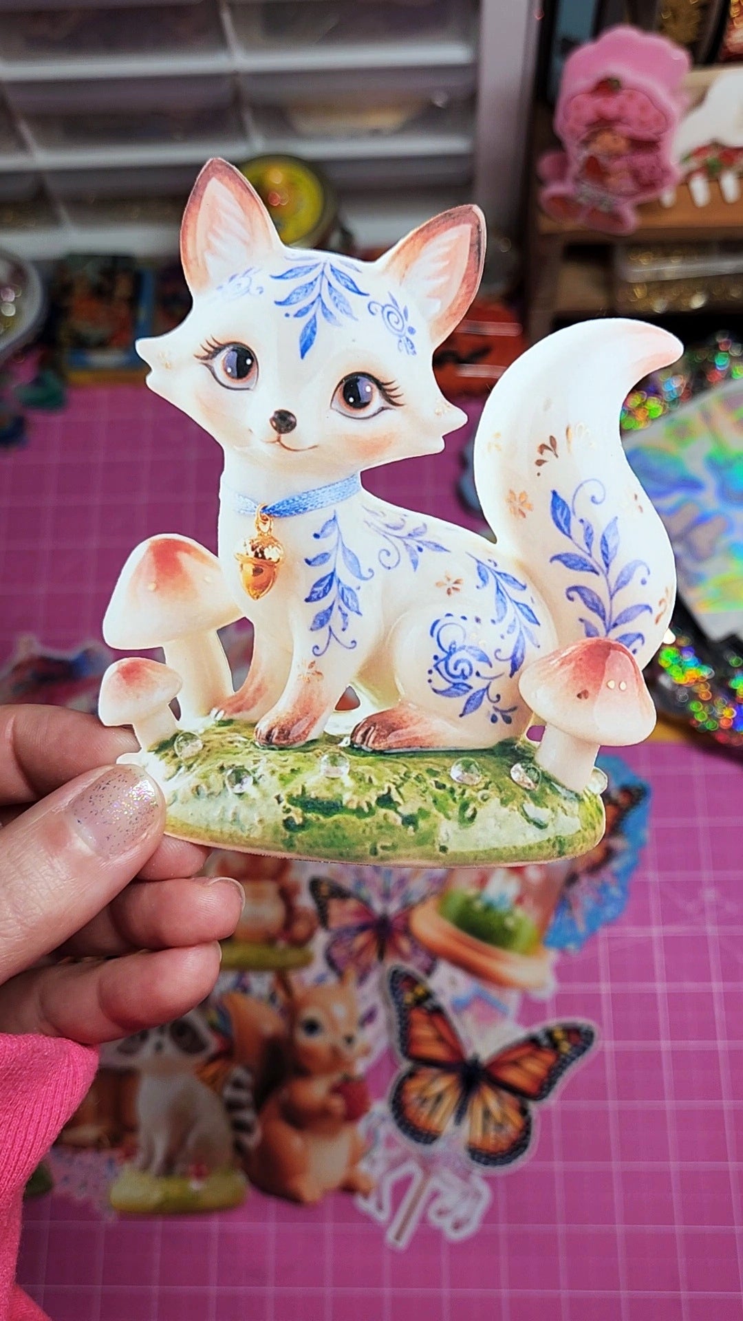 Decorative figurine of a fox with floral patterns held by a hand on a colorful background.