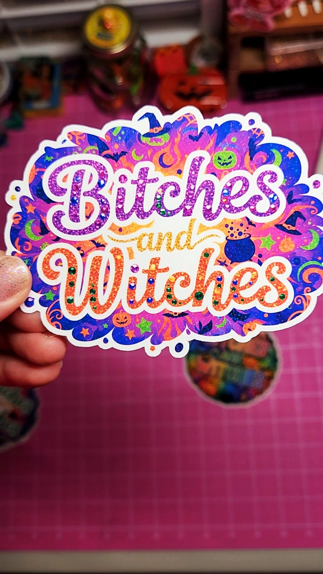 Colorful sticker with 'Bitches and Witches' text held over a pink background