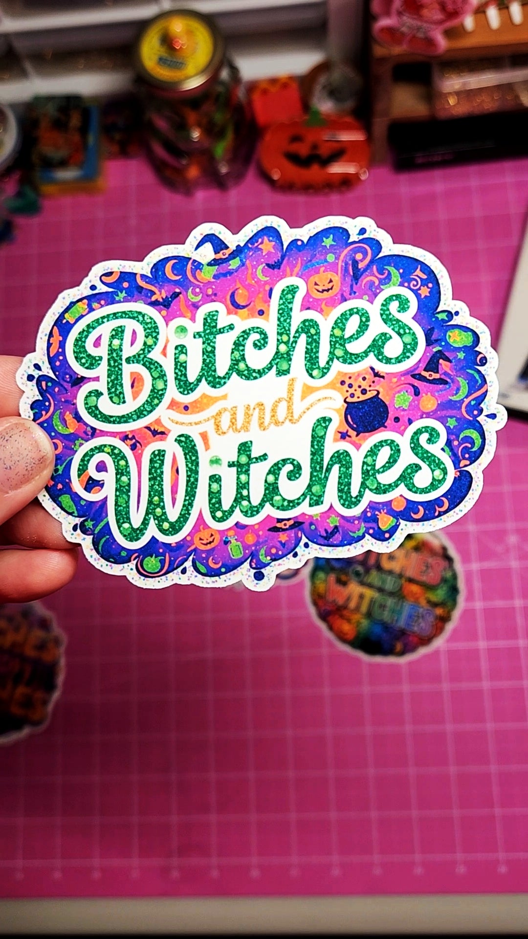 Sticker with 'Bitches and Witches' text held over a pink grid background