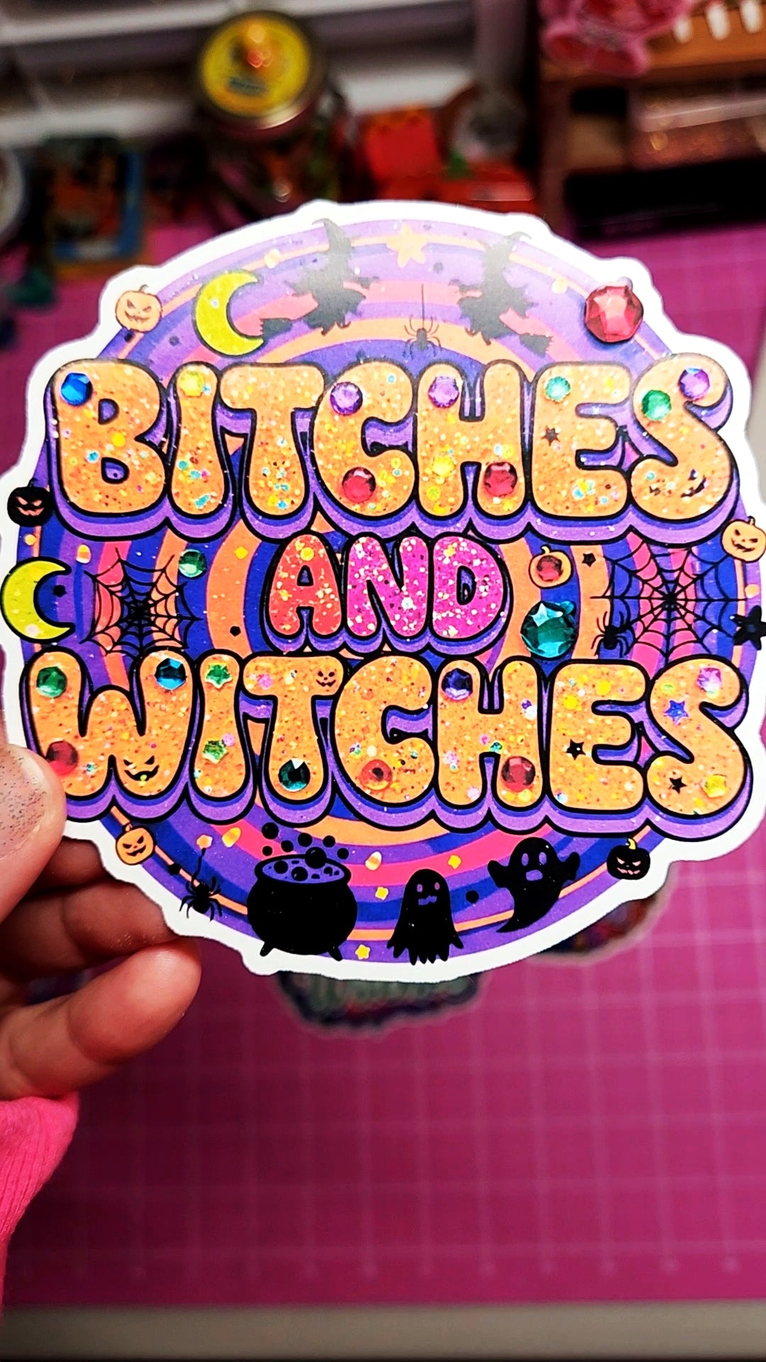 Colorful sticker with text 'Bitches Candy Witches' held by a hand on a pink surface.