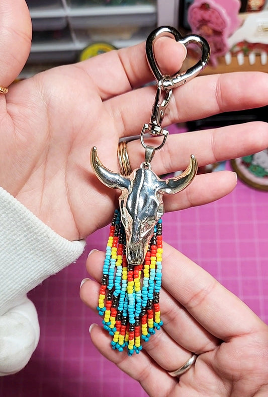 Keychain with bull head design and colorful beads held by a hand against a pink background.