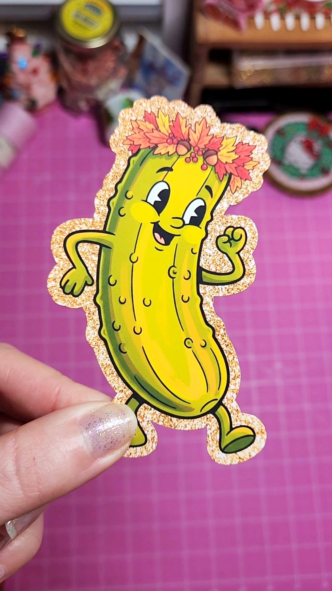 Cartoon pickle with a flower crown held by a hand on a pink background