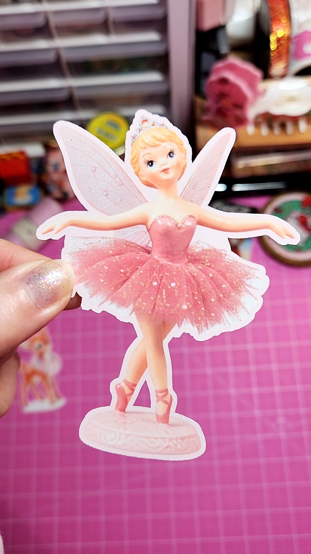 Fairy figurine in a pink dress held by a hand on a pink background