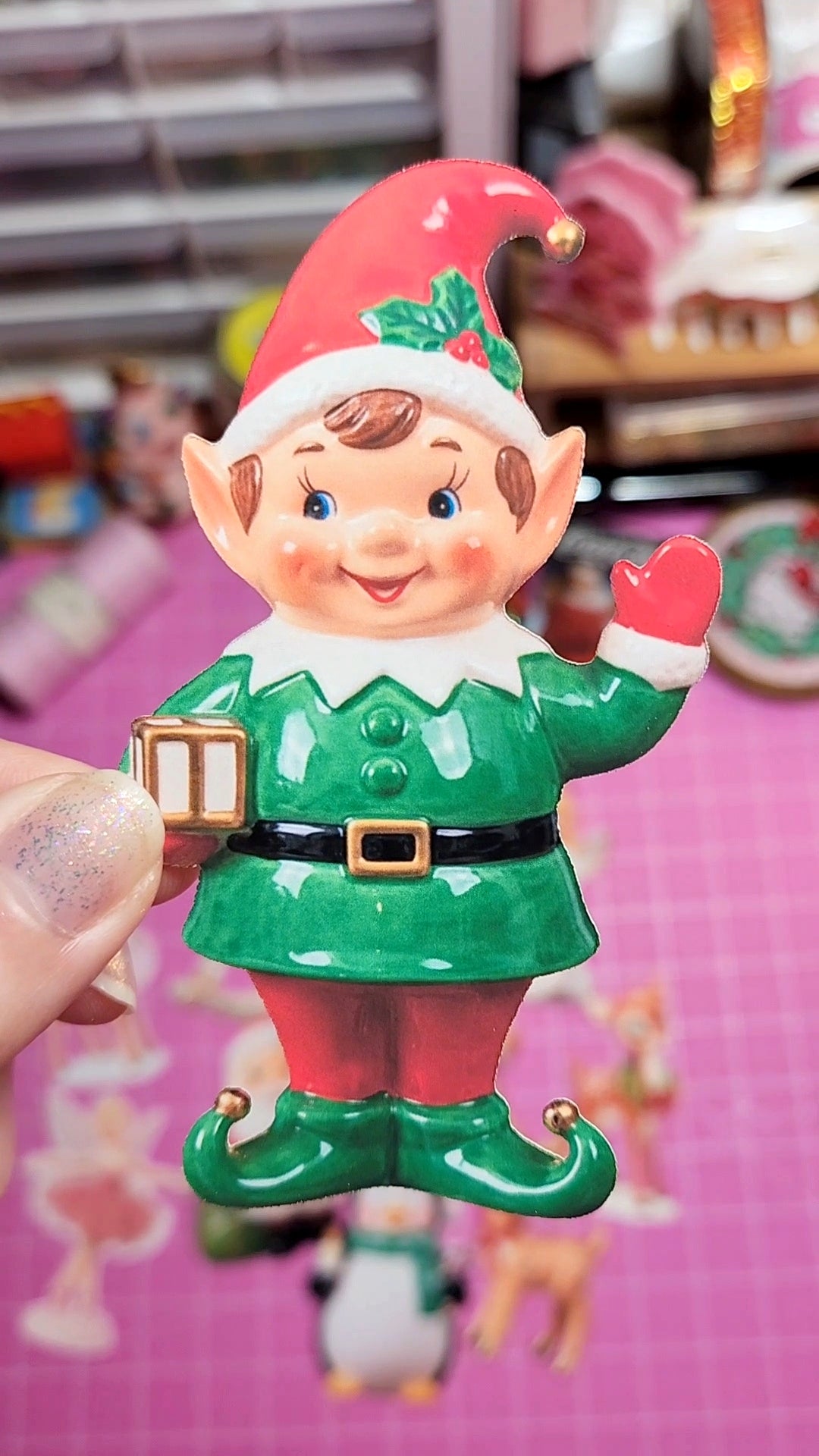 Elf figurine with a red hat and green outfit on a pink background