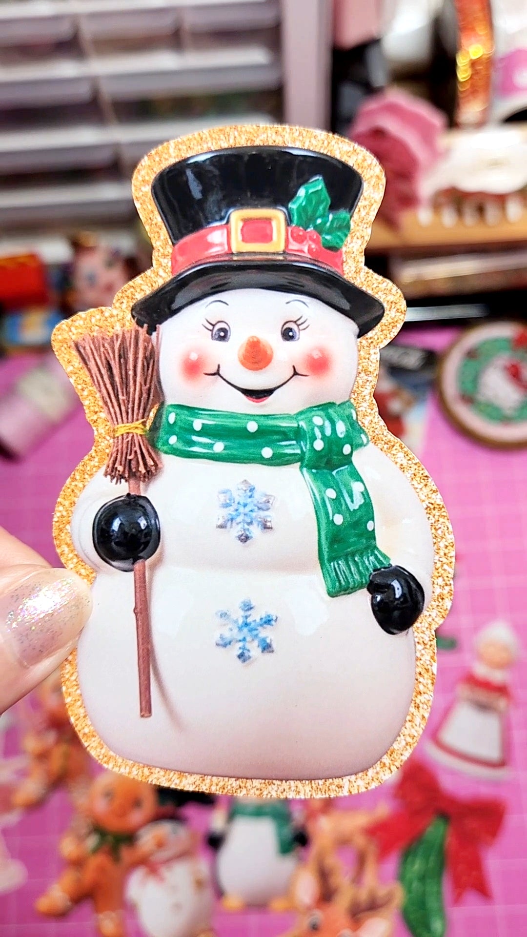 Decorative snowman ornament with a colorful hat and scarf, held against a blurred festive background.