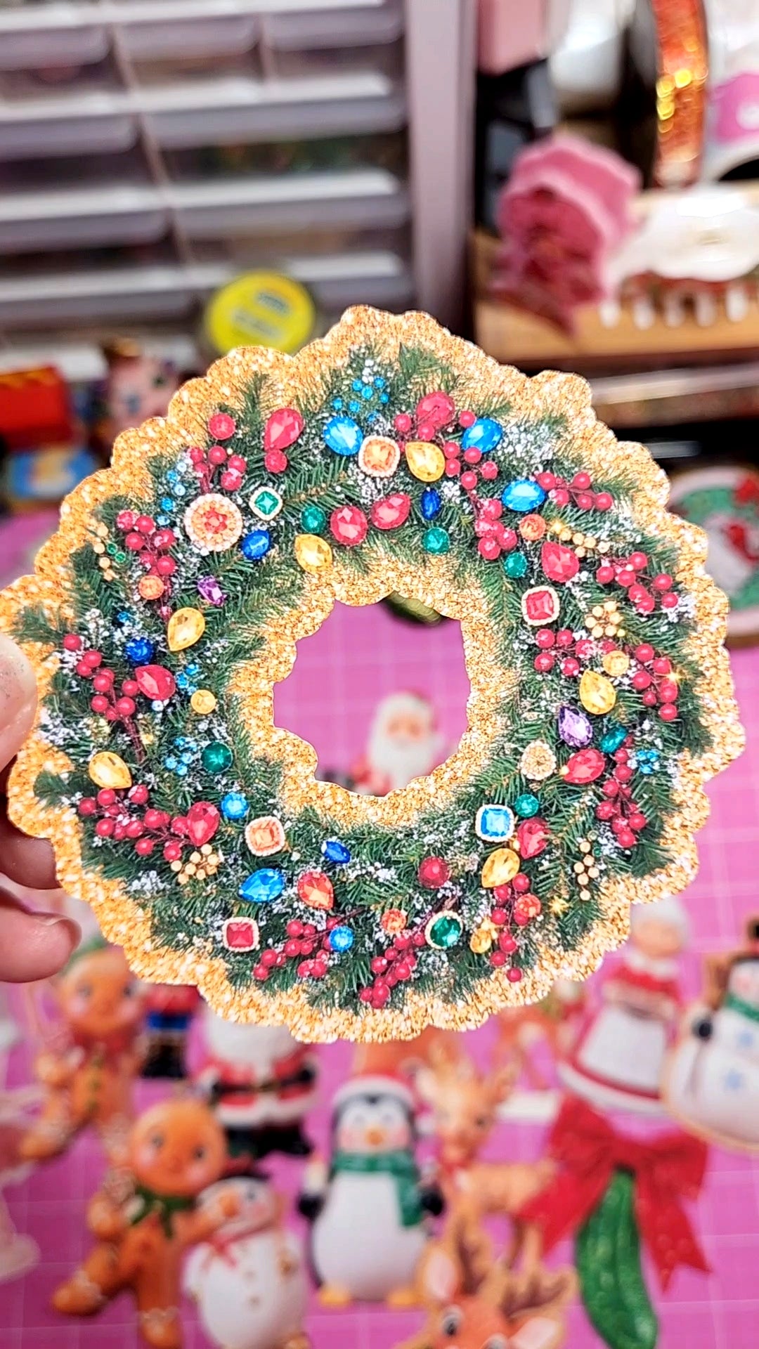 Decorative Christmas wreath with colorful ornaments held in front of a colorful background with cartoon characters.