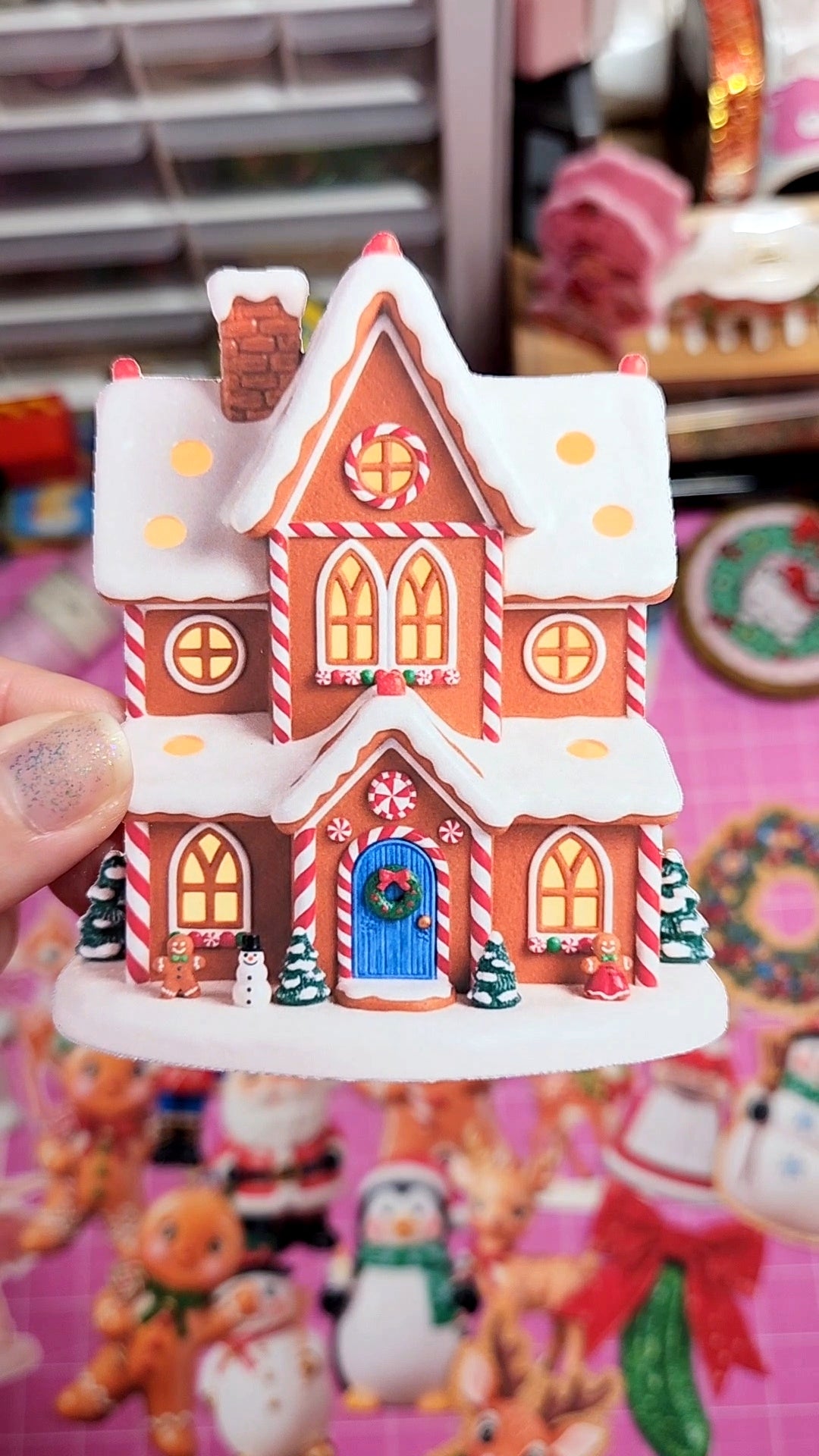Decorative gingerbread house toy held in front of a colorful background with Christmas-themed items.