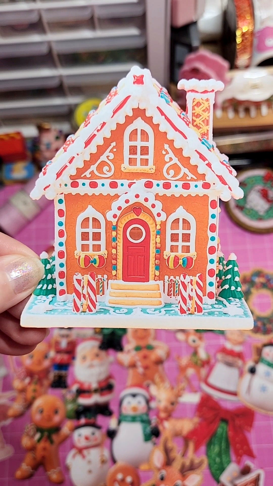 Decorative gingerbread house sticker held in front of a colorful background with Christmas-themed figures.