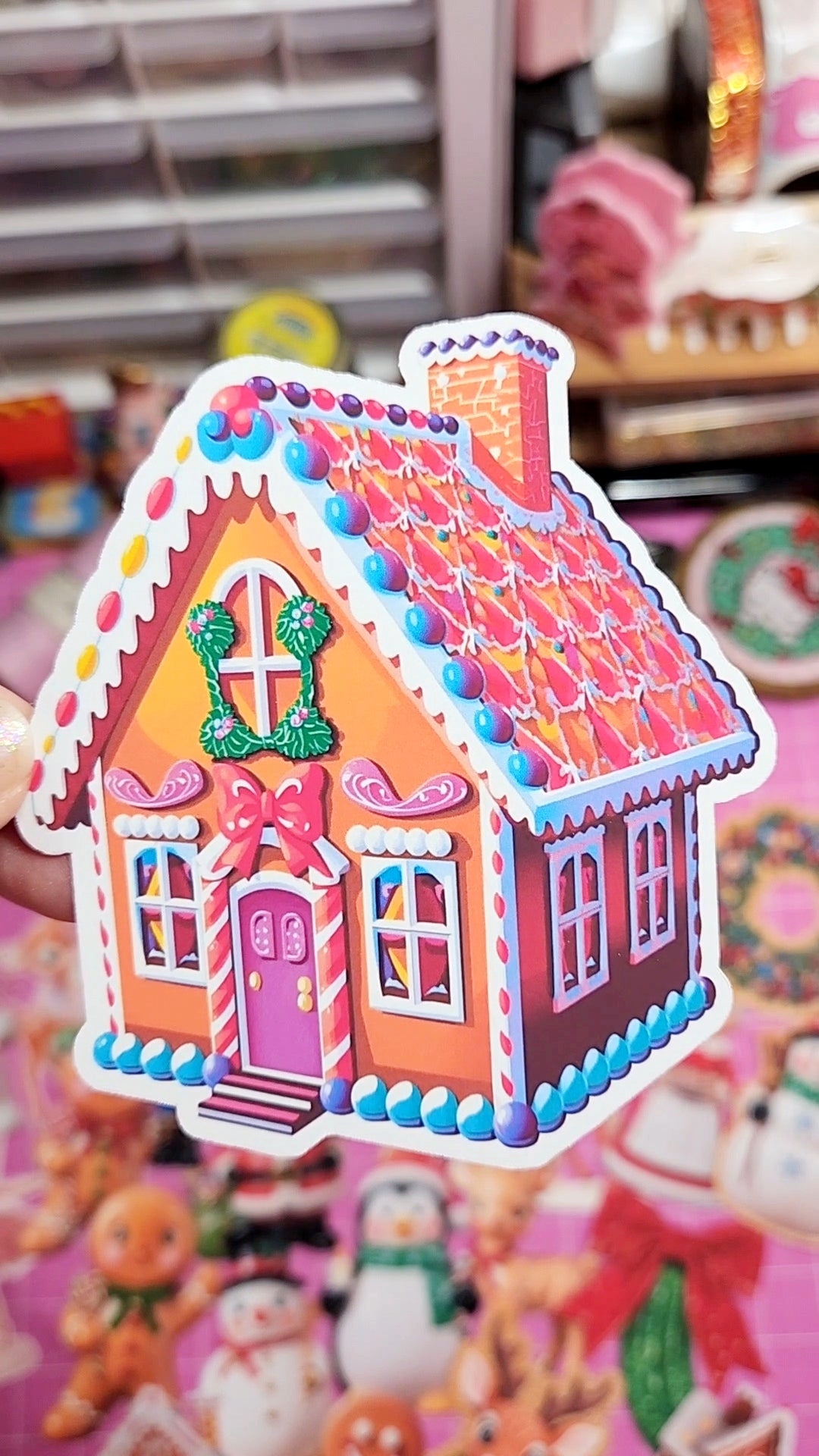 Colorful gingerbread house sticker on a busy background with toys and decorations.